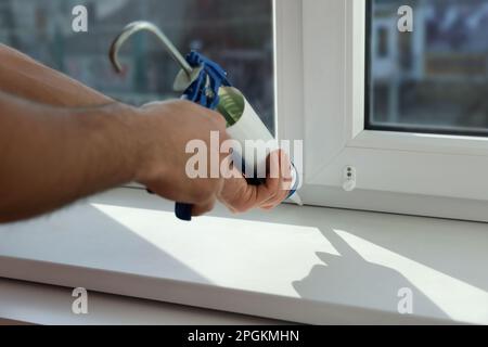 Man versiegelt Fenster mit Abdichtung drinnen, Nahaufnahme Stockfoto