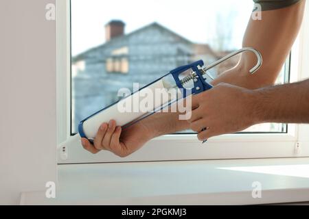 Man versiegelt Fenster mit Abdichtung drinnen, Nahaufnahme Stockfoto