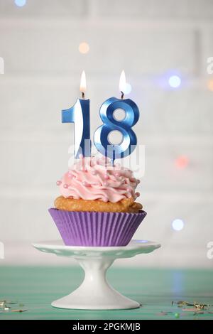 Zum 18. Geburtstag. Köstlicher Cupcake mit zahlenförmigen Kerzen für eine Party auf einem türkisfarbenen Tisch Stockfoto