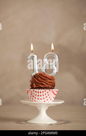 Zum 18. Geburtstag. Köstlicher Cupcake mit zahlenförmigen Kerzen für eine Party auf einem beigen Tisch Stockfoto