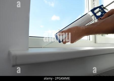 Man versiegelt Fenster mit Abdichtung drinnen, Nahaufnahme Stockfoto