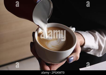 Der Barista gießt aufgeschäumte Milch aus dem Pitcher in eine Tasse aromatischen Kaffees im Café Stockfoto