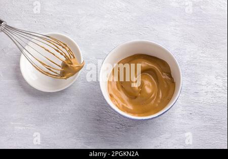 Keramikschüssel und Schneebesen mit flauschigem, cremigem Kaffeeschaum auf hellgrauem, strukturiertem Hintergrund. Für Dalgona-Kaffee, trendiges Speise- und Getränkekonzept Stockfoto