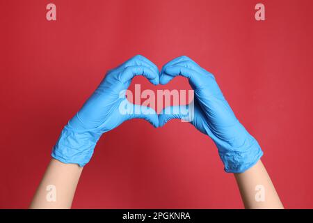 Arzt in medizinischen Handschuhen, die Herz mit Händen auf rotem Hintergrund machen, Nahaufnahme Stockfoto