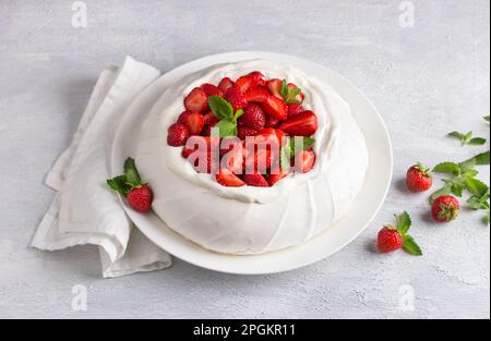 Klassischer Pavlova-Baiser-Kuchen mit Schlagsahne und Erdbeeren, gestreut mit Puderzucker auf hellgrauem, strukturiertem Hintergrund, selektiver Fokus Stockfoto