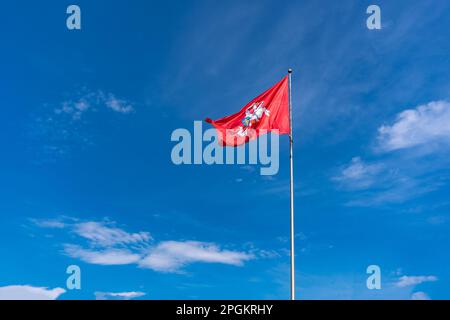 Die historische Flagge Litauens, ein Reiter mit einem Schwert auf einem weißen Pferd auf rotem Hintergrund flattert vor einem hellblauen Himmel mit weißen Wolken Stockfoto