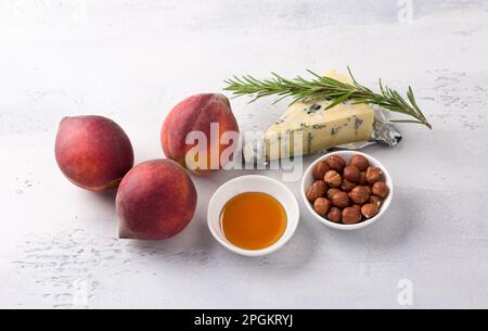 Zutaten für gebackene Pfirsiche: Frische Pfirsiche, Blauschimmelkäse, Haselnüsse, Honig und Rosmarin auf hellgrauem Hintergrund, Draufsicht Stockfoto
