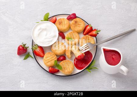 Hausgemachte Hüttenkäse-Gnocchi mit Erdbeersauce, frischen Erdbeeren und Sauerrahm, dekoriert mit Minze auf hellgrauem Hintergrund, Top vi Stockfoto