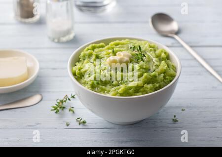 Zarter Kartoffelpüree mit grünen Erbsen, aromatisiert mit Butter, Gewürzen und Thymian auf hellblauem Hintergrund. Köstliches hausgemachtes Essen Stockfoto