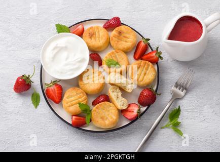 Hausgemachte Hüttenkäse-Gnocchi mit Erdbeersauce, frischen Erdbeeren und Sauerrahm, dekoriert mit Minze auf hellgrauem Hintergrund, Top vi Stockfoto