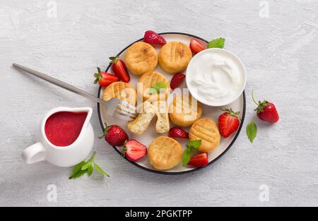 Hausgemachte Hüttenkäse-Gnocchi mit Erdbeersauce, frischen Erdbeeren und Sauerrahm, dekoriert mit Minze auf hellgrauem Hintergrund, Top vi Stockfoto