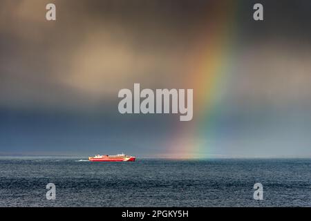 Die Fähre Gills Bay nach Orkney, der MV Alfred, unter stürmischem Himmel und Regenbogen, auf dem Pentland Firth, nahe John O'Groats, Caithness, Schottland, Großbritannien. Stockfoto