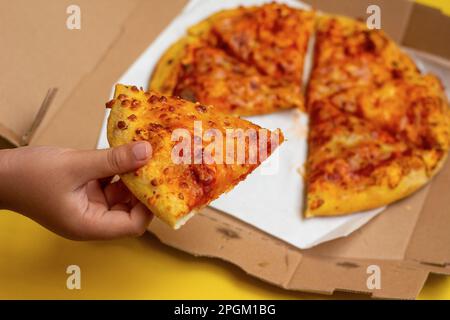 Hand, die ein Stück Pizza aus einer Pizzaschachtel nimmt Stockfoto