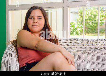 Ruhe und Frieden zu Hause, Porträt einer jungen Latina-Frau, argentinischer Herkunft, mit bequemen Kleidern, langen Haaren und weißem Leder, entspannen Stockfoto