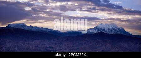Der Blick auf den schneebedeckten Illimani-Berg mit Wolken, die bei Sonnenuntergang über dem Gipfel schweben. Bolivien. Stockfoto