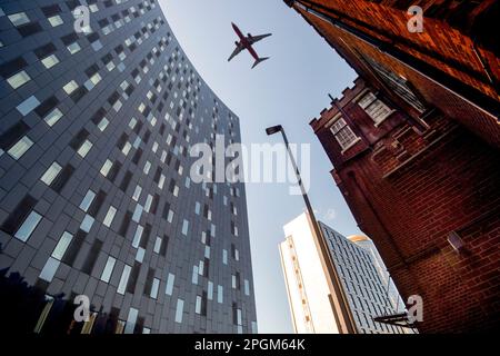 Blick aus dem niedrigen Winkel auf das Flugzeug über Wolkenkratzer und Gebäude. Stockfoto