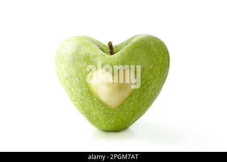 Grüner Apfel mit halbgefressener Herzform in der Mitte, reflektiert auf weißem Tisch und weißem isoliertem Hintergrund. Gute Gesundheit, Ernährung und Wellness Konz Stockfoto