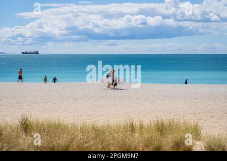 Tauranga Neuseeland - März 22 2023: Mo. Maunganui Hauptstrand im Hintergrund mit Menschen, die Surfbrett tragen. Stockfoto