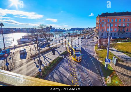 BUDAPEST, UNGARN - 22. FEBRUAR 2022: Verkehr am Angelo Rotta Ufer mit Blick auf die Donau und Silhouette des Parlamentsgebäudes am Horizont, ON Stockfoto