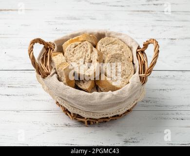 Vollständiges französisches Brot, Salzbrot oder Pistolenscheiben in einem Korb auf einem weißen Holztisch. Stockfoto