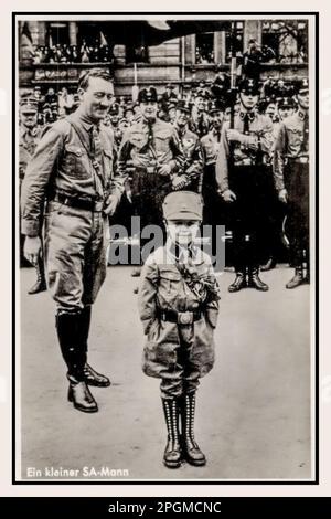 1930er Reichsparteitag Adolf Hitler in SA-Uniform schaut stolz auf einen kleinen Jungen 5-7years in voller Nazi SA Sturmabteilung Uniform Nürnberg, Nazi-Partei-Rallye, Nazi-Deutschland Foto Hoffmann, Hitlers bevorzugter Fotograf. Ein kleiner SA-Mann Stockfoto