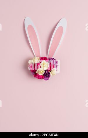 Hasen- oder Kaninchenohr mit Frühlingsblumen auf pastellrosa Hintergrund. Frohes Ostern-Minimalkonzept. Flach verlegt. Stockfoto