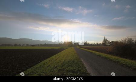 Fußweg bei Sonnenuntergang neben dem großen Feld Stockfoto