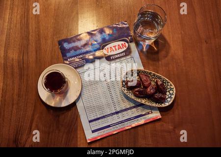 Hamburg, Deutschland. 23. März 2023. Ein Glas Wasser, ein Glas Tee, eine Schüssel Datteln und der Ramadan-Kalender mit den Zeiten liegen auf dem Tisch im Restaurant Pamukkale Köz. Der muslimische Fastenmonat Ramadan beginnt in diesem Jahr am 23. März und endet am 20. April. Kredit: Georg Wendt/dpa/Alamy Live News Stockfoto