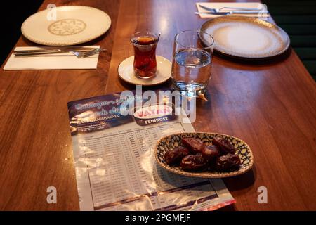 Hamburg, Deutschland. 23. März 2023. Ein Glas Wasser, ein Glas Tee, eine Schüssel Datteln und der Ramadan-Kalender mit den Zeiten liegen auf dem Tisch im Restaurant Pamukkale Köz. Der muslimische Fastenmonat Ramadan beginnt in diesem Jahr am 23. März und endet am 20. April. Kredit: Georg Wendt/dpa/Alamy Live News Stockfoto