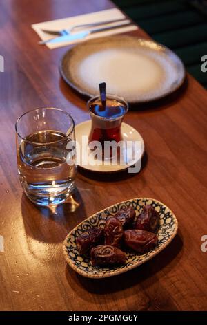 Hamburg, Deutschland. 23. März 2023. Ein Glas Wasser, ein Glas Tee und eine Schüssel Datteln liegen im Restaurant Pamukkale Köz auf dem Tisch. Der muslimische Fastenmonat Ramadan beginnt in diesem Jahr am 23. März und endet am 20. April. Kredit: Georg Wendt/dpa/Alamy Live News Stockfoto