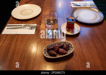 Hamburg, Deutschland. 23. März 2023. Ein Glas Wasser, ein Glas Tee und eine Schüssel Datteln liegen im Restaurant Pamukkale Köz auf dem Tisch. Der muslimische Fastenmonat Ramadan beginnt in diesem Jahr am 23. März und endet am 20. April. Kredit: Georg Wendt/dpa/Alamy Live News Stockfoto