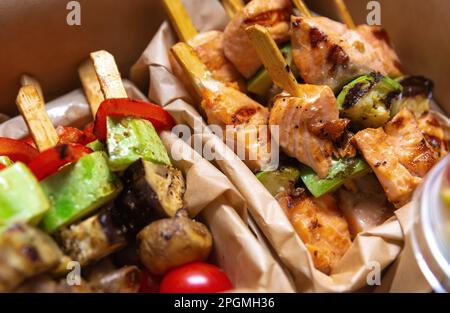 Gegrilltes Lachsfilet und Gemüse auf Spießen gekocht und zum Mittagessen in einer Schachtel geliefert. Köstliche natürliche Mahlzeit für Pescatarier oder Flexitarian di Stockfoto