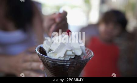 Ein kleiner Junge isst Schokoladeneis mit chantilly Schlagsahne oben drauf. Kind und Mutter essen nach dem Mittagessen süßes Dessert Stockfoto