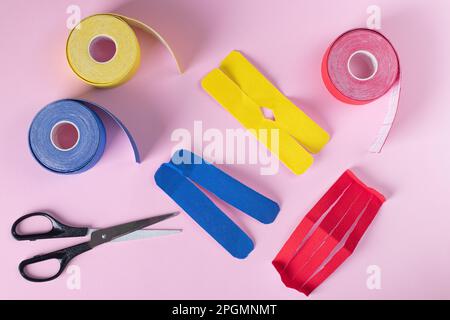 Farbenfrohes kinesiologisches Klebeband, Schere und unterschiedlich geformte Schnitte für Applikation auf pinkfarbenem Hintergrund, Draufsicht Stockfoto