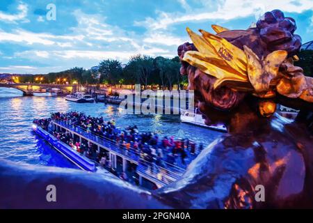 Das Vergnügungsboot fährt schnell auf der seine - beleuchtet in der Dämmerung auf der Pont Alexander 3. Unscharfe Bewegungen. Stockfoto