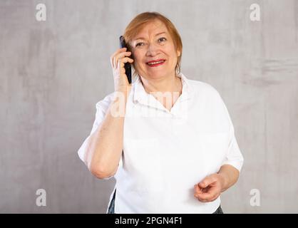 Ältere Frau, die am Telefon mit Stolz und einem glücklichen selbstbewussten Grinsen spricht Stockfoto