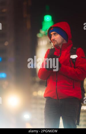 Ein junger Mann in einer roten Jacke, der in einer Stadtstraße steht und zur Seite schaut Stockfoto