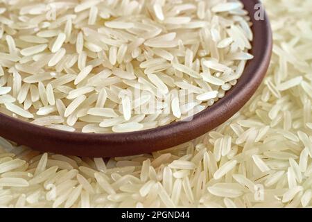 Gesunder Basmati-Reis in einer Tonkeramikschüssel Nahaufnahme vor dem Hintergrund verstreuter Reiskörner Stockfoto