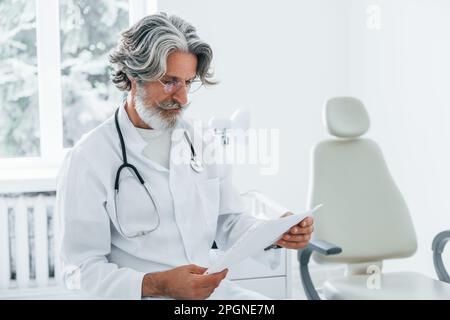 Das Porträt eines erfahrenen Arztes mit grauem Haar und Bart im weißen Kittel ist in der Klinik Stockfoto