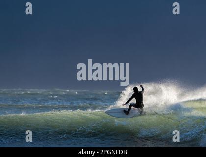 Junger Mann balanciert mit Surfbrett auf Wellen im Meer Stockfoto