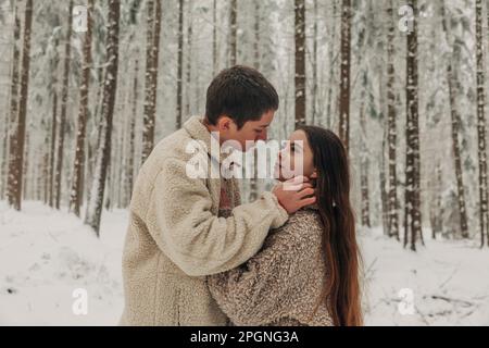 Ein romantisches Teenager-Paar, das im verschneiten Wald zusammensteht Stockfoto