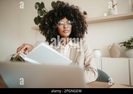 Nachdenkliche Geschäftsfrau mit Brille, die mit einem Buch im Büro sitzt Stockfoto