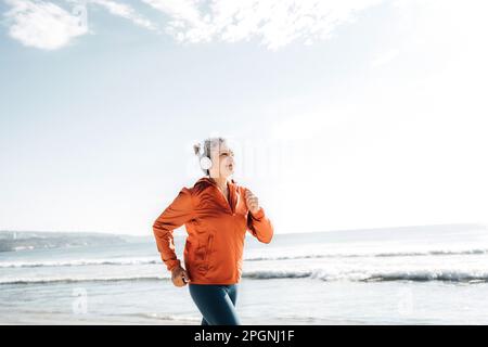 Lächelnde Frau mit Kopfhörern beim Joggen am Strand Stockfoto