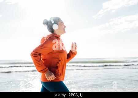 Frau mit Kopfhörern, die an sonnigen Tagen auf dem Meer joggt Stockfoto