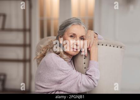 Seniorin sitzt zu Hause auf einem Stuhl Stockfoto
