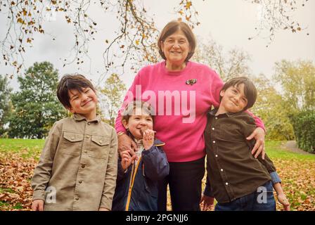 Lächelnde Seniorin, die mit ihren Enkeln im Park steht Stockfoto