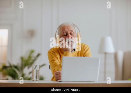 Freiberufler trägt kabellose Kopfhörer und arbeitet auf einem Laptop Stockfoto