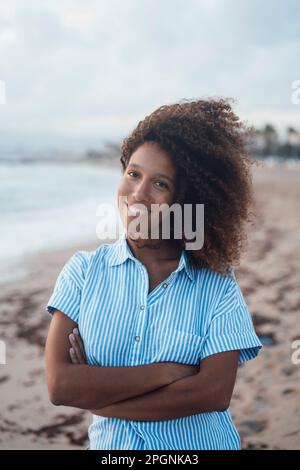 Glückliche junge Frau mit gekreuzten Armen, die am Strand stand Stockfoto