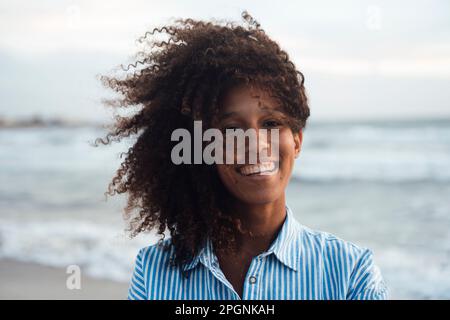 Glückliche junge Frau mit lockigem Haar am Strand Stockfoto