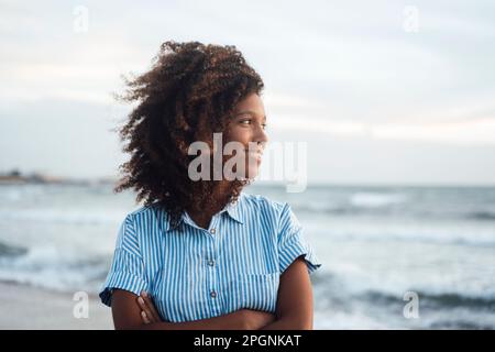 Glückliche junge Frau mit verschränkten Armen, die vor dem Meer steht Stockfoto